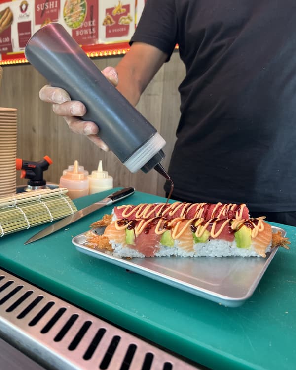 Onze chef trekt saus over een afgewerkte signature roll in de kraam, naast het mes en de bamboemat
