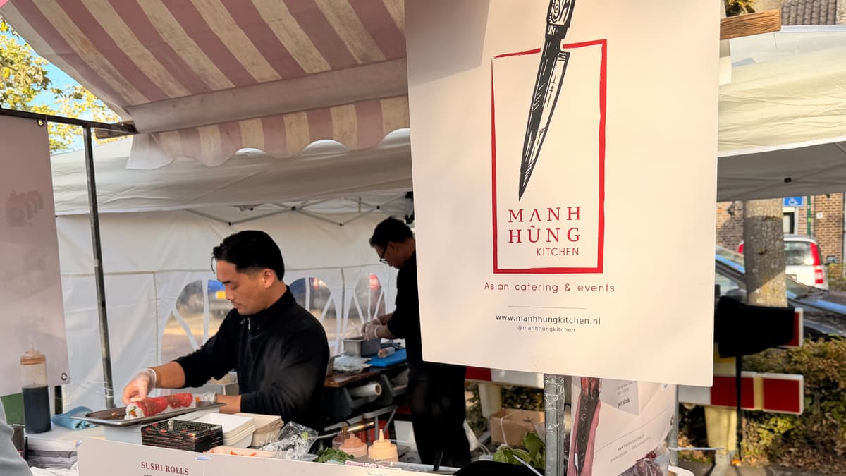 Onze kraam op de markt, met de banner van Mạnh Hùng Kitchen en twee chefs aan het werk