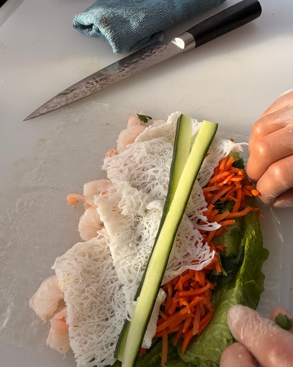 Een zomerrolletje in opbouw: garnalen, rijstvermicelli, komkommer en wortel, met het mes van de chef ernaast