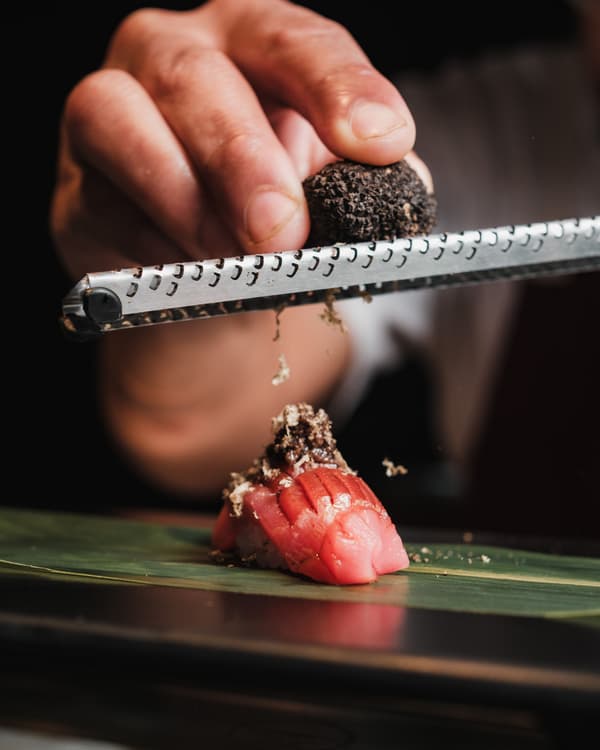 De chef raspt zwarte truffel over een stuk tonijnnigiri op een bananenblad