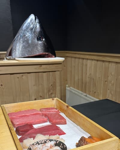 Een kist met blokken tonijn aan de sushitoonbank, met een tonijnkop op de plank erachter