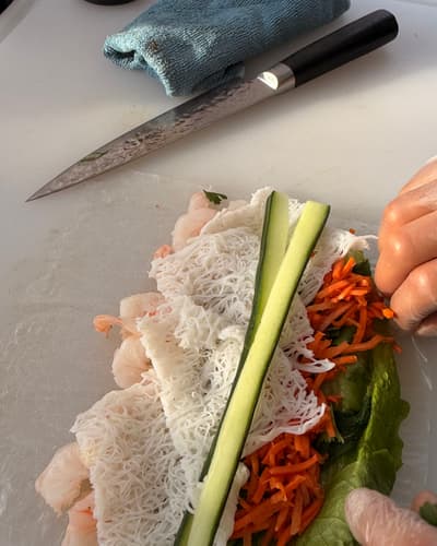 Garnalen, rijstvermicelli, komkommer, wortel en sla plat gelegd op rijstpapier, met het mes van de chef ernaast