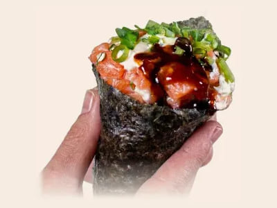 Een hand roll met zalm, bosui en saus, vastgehouden in de hand